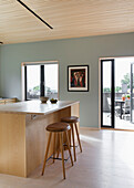 Küchentheke mit hellen Holzfronten und Barhockern, Blick auf die Terrasse