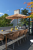 Long wooden table with fruit and refreshments, rattan chairs and umbrella on the roof terrace