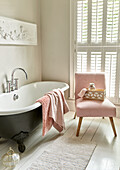 Bathroom with freestanding bathtub and pink upholstered chair