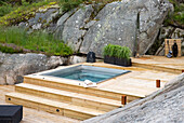 Wooden terrace with hot tub and shower, surrounded by rocks and flower beds