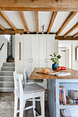 Country kitchen with light grey centre block and wooden beamed ceiling