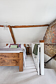 Double bed in the attic bedroom with wooden beams, exposed brickwork and staircase