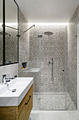 Bathroom in a single young man apartment, gray with stoneware tiles imitating cement tiles from the early 20th century in the shower, mirror cabinets above the washbassin