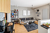 Single young man apartment, living room connected with open kitchen, gray colors combined with light walnut wood, light oak floor panels on the floor matching the color of the cabinet fronts, black male accents in furniture and decorations