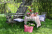 Garden table with spring flowers and Gugelhupf, bag with tulips in the grass