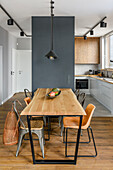 Kitchen in subdued colors of shades of gray and warm natural wood. Hanging cabinets, countertop and shelves made of oak wood, large-format stoneware tiles on the floor, imitating concrete. Dinning table with industrial style chairs and lamps hanging