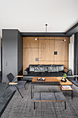 Living room in black and dark brown, wall above leather couch covered with oak veneer