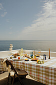 Gedeckter Tisch mit karierter Tischdecke auf Terrasse mit Meerblick