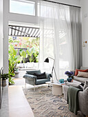 Helles Wohnzimmer mit bodenlangen Gardinen, Blick auf Terrasse mit Pflanzen
