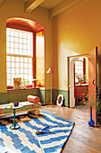 Gelbes Zimmer mit blau-weißem Teppich und bunter Bank