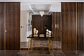 Hallway in dark brown color palette with gold accessories, walls, and wardrobes in dark oak, large format stoneware tiles, console, and wall mirror