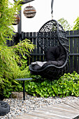 Black rattan hanging chair with cushions in a modern garden area