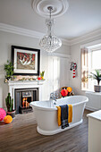 Freestanding bathtub in bathroom with chandelier, fireplace and plants