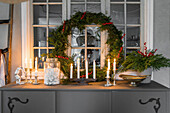Festliche Weihnachtsdekoration mit Kerzen und Kranz auf einer Anrichte