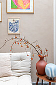 Vase mit Zweigen und kleinen orangenen Früchten neben cremefarbenen Sofa