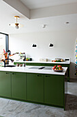 Modern kitchen with green base units and golden pendant light