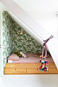 Cot with storage space and jungle wallpaper under sloping ceiling