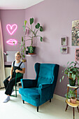 Wall in purple, neon signs in heart and lip shape, wing chair in blue and houseplants