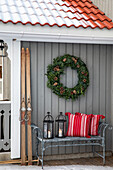Metal bench with red cushions, Christmas wreath and nostalgic skis on the wall of the house