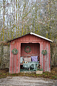 Red wooden garden hut with blankets, cushions and homemade wreaths
