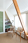 Rattan chair and vintage suitcases in room with sloping ceiling