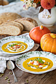 Pumpkin soup in soup bowls garnished with pumpkin seeds and parsley, bread and pumpkins