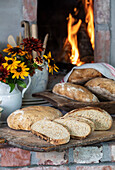 Frisch gebackenes Brot und Herbstblumen vor Kaminfeuer