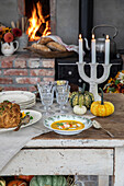 Gedeckter Tisch mit Kürbissen vor Ofen im rustikalen Stil