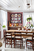 Dining area with wooden table, rustic chairs and wall shelf with plates