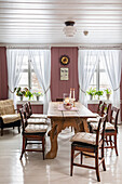Wooden dining table with chairs, white ceiling beams, walls in antique pink