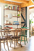 Wooden shelves with books and decorations, dining area with wooden table, brown wooden chairs and a green wooden chair