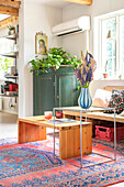 Grüner Schrank, Holztisch, Beistelltisch mit Chromfüßen, Blumenstrauß in Vase, Vintage-Teppich