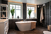 Freestanding bathtub in modern bathroom with dark tiles