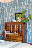 Antique secretary and wooden chair in front of blue wallpaper with floral patterns in the bedroom