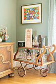 Wooden serving trolley with spirits and carafes, colorful art on wall