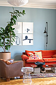 Wohnzimmer mit orange-rotem Sofa, blauer Wand und großer Zimmerpflanze