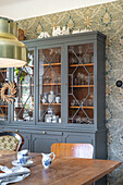 Display cabinet in the dining room with floral wallpaper and retro crockery