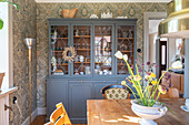 Dining room with display cabinet, patterned wallpaper and wooden table