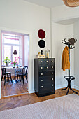 Hallway with herringbone parquet flooring, coat rack, black chest of drawers and carpet, view of dining area