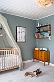 Children's room with blue walls, wooden furniture and cot with canopy