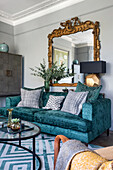 Blue velvet sofa with cushions and an antique mirror above in a living room