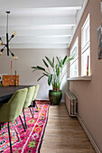 Dining room with green velvet chairs and oriental rug, houseplant by the window