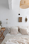 Light-coloured bedroom with beige bed linen and rattan ceiling lamp