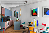 Küche, ovaler Esstisch mit bunten Stühlen und moderne Kunst an der Wand in offenem Wohnraum