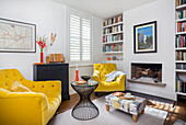 Bright living room with sofa and armchair in yellow, fireplace and bookshelves