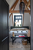 Double bed with black wooden bench with decoration in front and black hanging lamp in the bedroom
