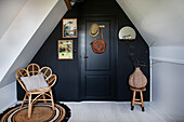 Flower-shaped rattan armchair in front of black-painted wall and door in the attic