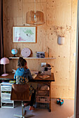 Girl at a desk in children's room with light-colored wood paneling