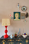 Red table lamp, bowls and candles on a painted sideboard