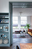 Durchgang mit grau-blauen Holzvertäfelung, daneben Einbauregal, mit Blick ins Wohnzimmer